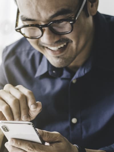 Person in glasses smiles while using their cell phone.